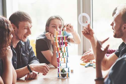 a group of creative friends sitting on a wooden table. people were having fun while playing a board game.